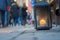 Big metal dirty lantern with burning candle inside, outdoor on a ground with blurred crowded street on a background.