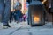 Big metal dirty lantern with burning candle inside, outdoor on a ground with blurred crowded street on a background.