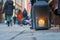 Big metal dirty lantern with burning candle inside, outdoor on a ground with blurred crowded street on a background.