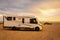 Big modern motorhome camper van parked on the ground and beautiful beach with sea and sunset lights in background. Concept of