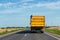 Big modern yellow grain hopper cargo truck driving on highway to silo granary storage unloading aginst clear blue sky on