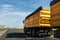 Big modern yellow grain hopper cargo truck driving on highway to silo granary storage unloading aginst clear blue sky on