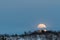 Big moon rising behind a mountain with some birch trees in winter landscape with snow, in Setesdal, Norway