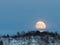 Big moon rising behind a mountain with some birch trees in winter landscape with snow, in Setesdal, Norway