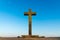 Big old Christian stone cross covered with bright yellow lichen in front of a clear blue sky at the beginning sunset