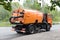 Big orange machine clears the asphalt with a sweeper near the curb