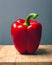 Big red bell pepper on a wooden stand on a gray background