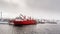 Big red cargo ship under the heavy snowfall in the port of Aasiaat, with village in the background, Greenland