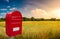 Big red cozy postbox with white empty note space for address is standing outdoor in front of beautiful countryside landscape at