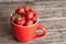 Big red cup filled with succulent juicy fresh ripe red strawberries on an old wooden textured table top with brick background