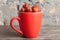 Big red cup filled with succulent juicy fresh ripe red strawberries on an old wooden textured table top with brick background