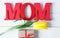 Big red letters Mom lies on the table with gift card and yellow tulips. Flowers for gift. Mother`s day concept.