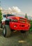 A big red monster truck with dirt tires standing on an off road against mountains and dramatic clouds