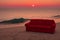 Big red sofa on shore of ocean, sea at sunset. Comfortable couch on sandy beach. Generative AI.