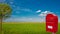 Big red stylish postbox with white empty note space for address is standing outdoor in front of beautiful countryside landscape