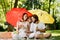 Big red and yellow umbrellas covering father, mother and children dressed in the in the white clothes from the bright