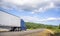 Big rig blue bonnet semi truck going with refrigerator semi trailer on the road with forest and meadows