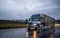 Big rig bonnet blue semi truck transporting cargo in covered bulk semi trailer running on the wet glossy road with raining weather