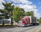 Big rig bright red classic semi truck with two covered semi trailers running on the local industrial road