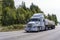 Big rig classic American semi truck transporting commercial cargo on flat bed semi trailer driving on wide multiline highway