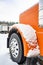 Big rig classic orange semi truck standing on the winter truck stop parking lot in row with another trucks covered by snow and ice