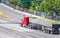 Big rig classic red semi truck transporting harvest of corn cobs in bulk semi trailer driving in the road intersection