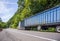 Big rig industrial semi truck with long bulk covered semi trailer driving on winding road with green forest