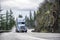 Big rig industrial semi truck tractor with loaded flat bed semi trailer turning on the wet mountain road at raining weather