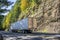Big rig long haul semi truck with refrigerated semi trailer driving on the autumn mountain road with rock wall and trees