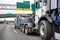 Big rig powerful tow semi truck towing broken truck on the lifting boom driving on the wide highway road with road signs and