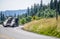 Big rig professional industrial car hauler semi truck driving on the winding road with green forest