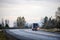 Big rig semi truck with black semi trailer driving on winding wet road in twilight evening time