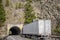 Big rig semi truck with refrigerator semi trailer moving on the road with tunnel through the rock