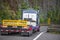 Big rig semi truck with sign oversize load behind flat bed semi trailer driving on the mountain road with rock wall on the side