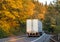 Big rig semi truck transporting semi trailer with cargo on winding road with yellow autumn trees in forest