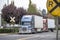 Big rig semi trucks with grille guard and reefer semi trailer standing on a railway crossing road in an industrial zone waiting