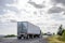 Big rig semi trucks transporting cargo in semi trailers running on the eveing local road
