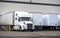 Big rig white semi truck with dry van semi trailer loading cargo in warehouse dock beside another semi trailers