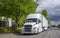 Big rig white semi truck with grille guard and refrigerator semi trailer parked on the city street near the warehouse