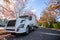 Big rig white semi truck with semi trailer standing on the road with autumn trees with leaves falling in the wind