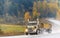 Big rig yellow gold tip truck with two tipper trailers running on autumn road in rain weather