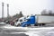 Big rigs semi trucks with different semi trailers standing for truck driver rest on the winter truck stop parking lot with snow