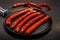 Big round black pan with five long fried hunting sausages