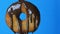 Big round donut on a fork on which chocolate icing glaze flows on a blue background