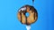 Big round donut on a fork on which chocolate icing glaze flows on a blue background