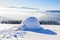 Big round igloo stands on mountains covered with snow.