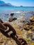 Big rusty ship chain, shallow blue water and rocky coastline