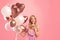 Big sale or special holiday offer. Happy young woman holding bunch of balloons, showing HUSH gesture on pink background