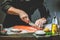 The big salmon is in the hands of the chef cook. He is using a knife to slice salmon fillet