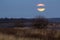 Big silver glowing Moon close-up on dark blue sky with scattered clouds.